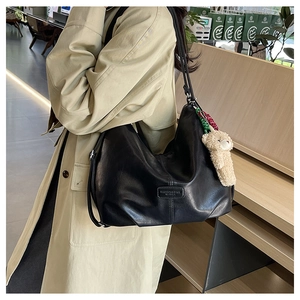 Detail view of black hobo bag with vertical stitching and cute plush bear charm accessory