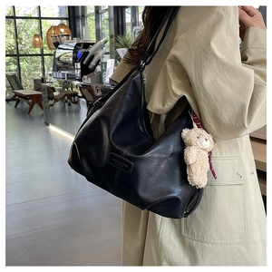 Detail of black soft leather tote bag featuring a cute cream plush bear pendant