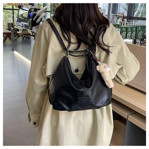 Detail of black PU leather hobo bag with teddy bear charm shown in a cozy cafe setting