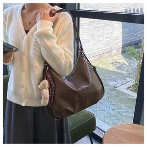 Detail of a dark brown half-moon hobo bag with a teddy bear charm and woven keychain