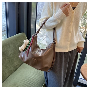 Detail of dark brown leather crescent tote bag with plush bear charm and woven strap
