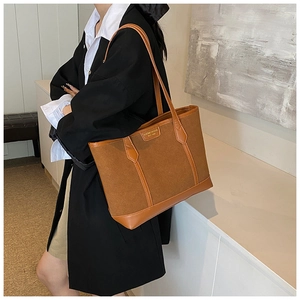 Detail of brown vintage suede tote bag with leather straps and logo plaque in model setting