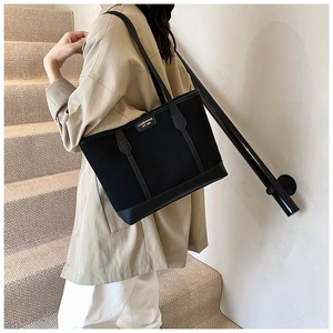 Detail of black matte tote bag with metallic logo plate worn by model in street style