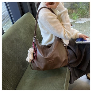 Detail of dark brown faux leather tote bag with plush bear charm on a green sofa