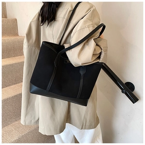 Detail of a large black tote bag with leather trim and LUOMEN logo on canvas fabric