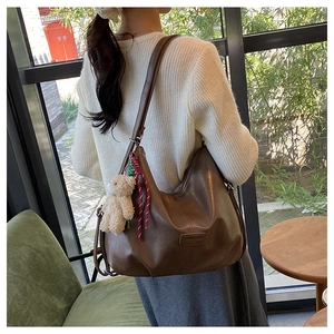 Brown leather hobo bag on shoulder with plush bear charm and woven cord detail