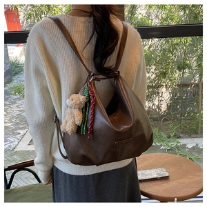 Detail of dark brown leather hobo bag with teddy bear charm and woven rope decoration