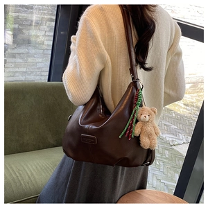 Detail of dark brown leather tote bag with cute bear charm and woven rope accessory