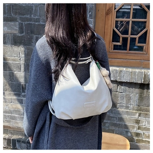 Detailed view of a white crescent Hobo bag worn by a model against a vintage brick wall