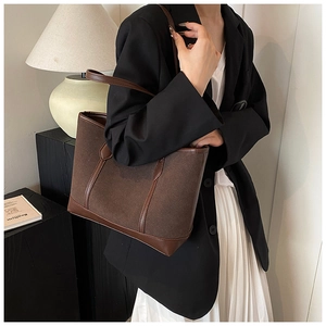 Brown frosted tote bag styled with black blazer and pleated skirt in a minimalist setting
