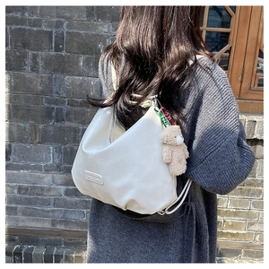 Detailed shot of white hobo bag with plush bear charm worn by model on shoulder