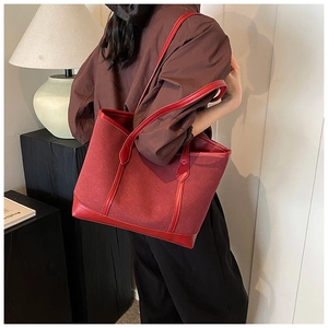 Side view of a red suede tote bag with leather trim worn by a model in a minimal studio