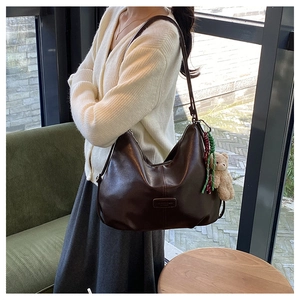 Detailed view of deep brown leather hobo bag with teddy bear charm on corduroy background