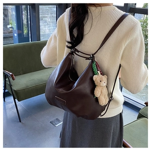 Detail of dark brown leather tote backpack with plush bear charm and woven tassel