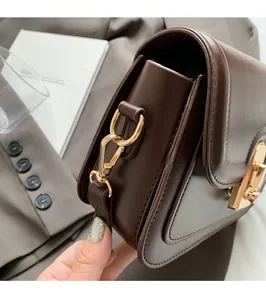 Détail d'un sac en cuir marron foncé avec ferrures dorées sur un costume gris