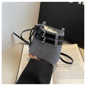 Détail d'un sac seau gris en daim mat avec des sangles noires et une fermeture à cordon