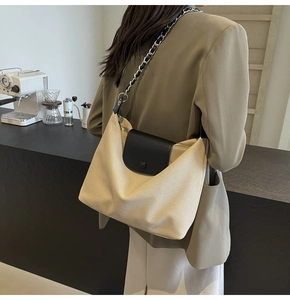 Detail of canvas tote bag with black leather flap and metal chain strap in urban cafe setting