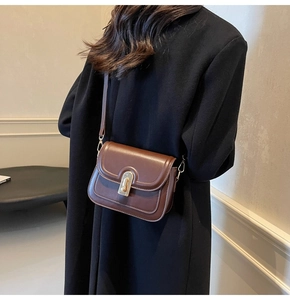 Sac bandoulière rétro en cuir marron avec boucle dorée porté sur un manteau noir