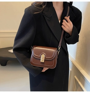 Détail d'un sac bandoulière en cuir marron foncé avec boucle dorée et surpiqûres