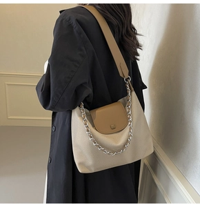 Detail of beige canvas tote bag with brown leather flap and silver chain on trench coat