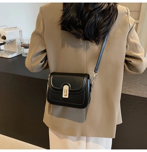 Détail d'un petit sac carré noir mat avec boucle dorée porté à l'épaule par un mannequin