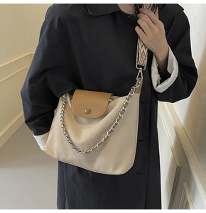 Detail of canvas and leather shoulder bag worn by model with patterned strap and metal chain