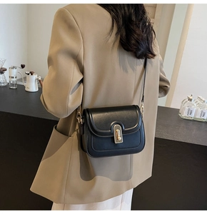 Détail du sac bandoulière noir avec fermoir tournant doré porté par un mannequin