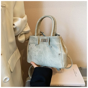 Detail of light grey-green denim handbag with metal twist lock and vintage rivets