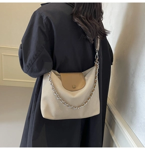 Close-up of beige woven tote bag with brown leather flap and silver chain strap