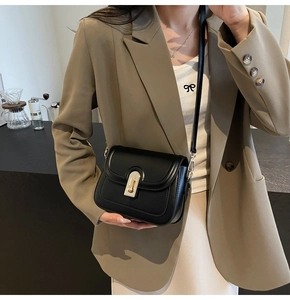 Détail d'un sac bandoulière carré en cuir noir avec boucle dorée porté par un mannequin