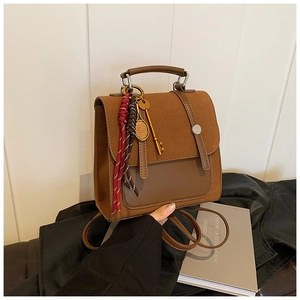 Detail of a brown patchwork backpack featuring woven cord pendants and metallic charms
