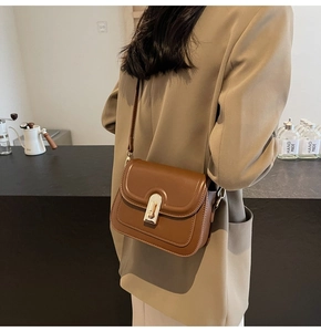 Détail du sac bandoulière marron caramel avec fermoir tournant doré sur un blazer