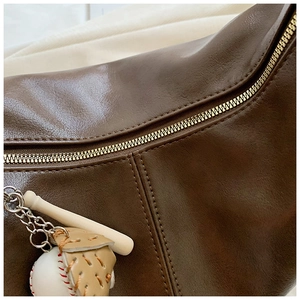 Detail of dark brown leather tote with metal zipper and baseball theme pendant charm