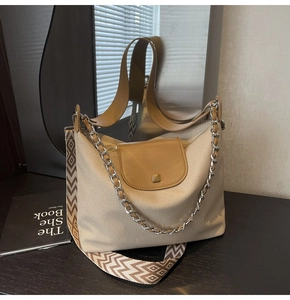 Detail of beige canvas tote bag with leather trim, metal chain and patterned strap