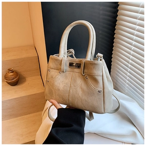 Close-up of beige faux leather handbag featuring denim pocket stitching and silver twist lock
