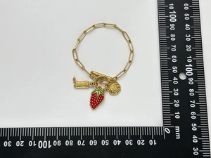 Détail d'un bracelet plaqué or 18K avec breloques coquillage, fraise et botte et fermoir OT