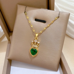 Detailed shot of a gold crown necklace with heart-shaped green gemstone on velvet
