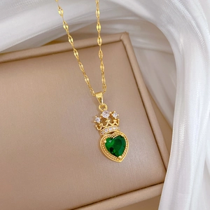 Detail of gold crown necklace with heart-shaped green crystal on a silk background