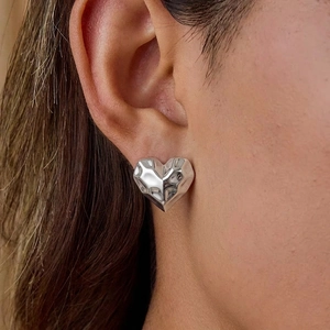Polished silver heart stud earrings with geometric faceted design on model's ear