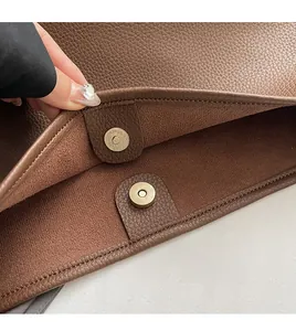 Macro shot of the magnetic metal clasp and litchi texture on brown leather bucket bag
