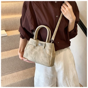 Detail of a beige canvas handbag with denim-style stitching and silver rivet accents
