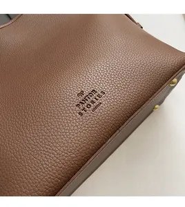 Detail of brown pebbled leather bag with embossed logo and golden metal rivets