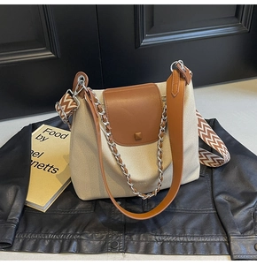 Detail of canvas tote bag with brown leather flap, metal chain and patterned strap