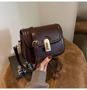 Détail d'un sac bandoulière en cuir marron foncé avec un fermoir rond en métal doré