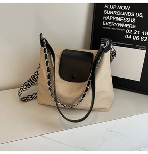 Detail of beige woven tote bag with black leather flap and geometric patterned strap