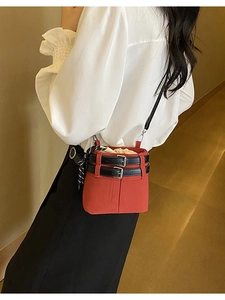 Mini sac seau rouge givré avec boucles noires porté par un mannequin dans un décor chaleureux