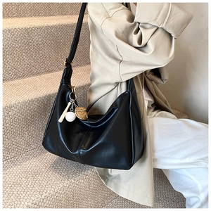 Detail of a large black faux leather hobo bag with baseball charm on a model