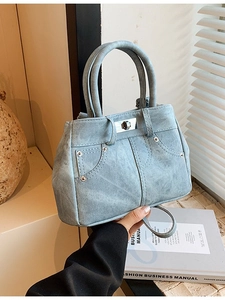 Light blue denim tote bag with metal studs and twist lock shown in a minimalist setting