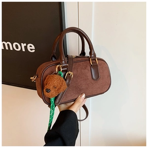 Détail d'un sac Boston en daim marron avec breloque chiot en peluche et corde verte