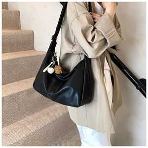 Detail of black leather hobo bag with a baseball charm on a beige staircase